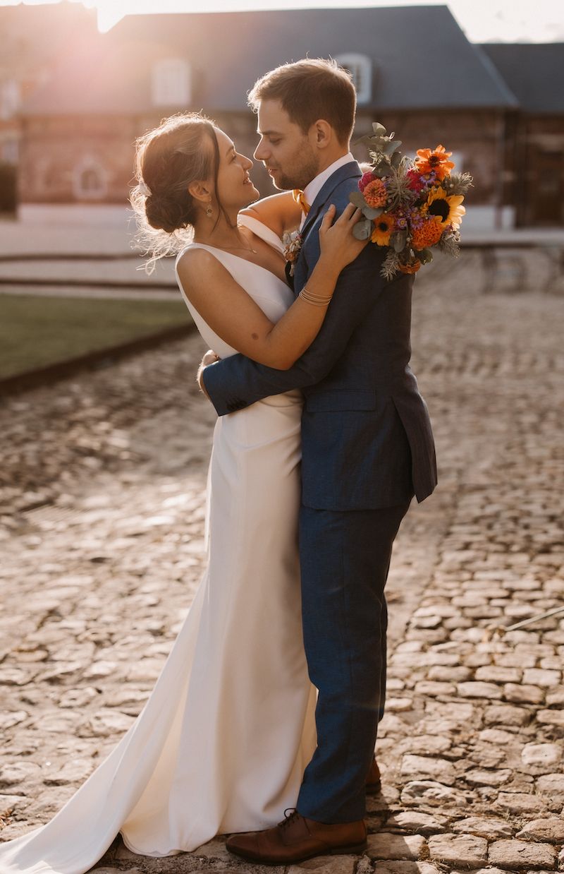 A romantic sunset embrace between newlyweds on cobblestone street with vibrant autumn bouquet.