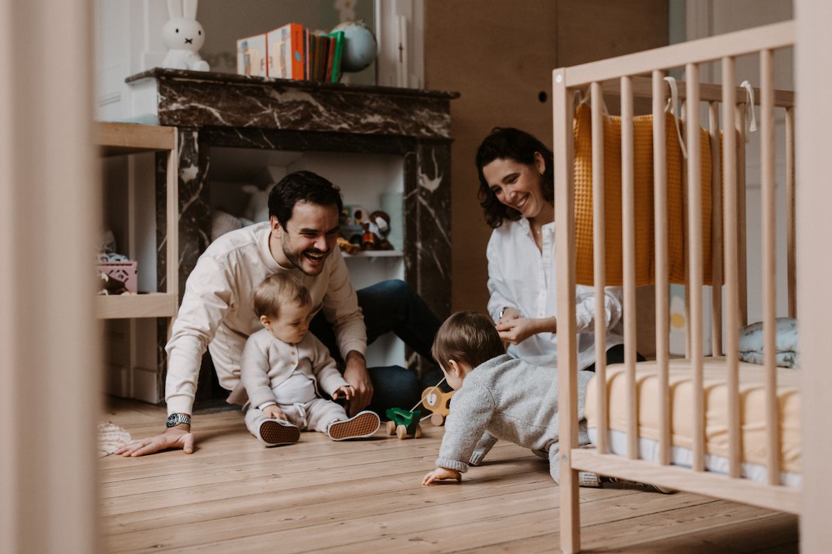 Family playing together on the floor next to a crib in a cozy nursery setting.