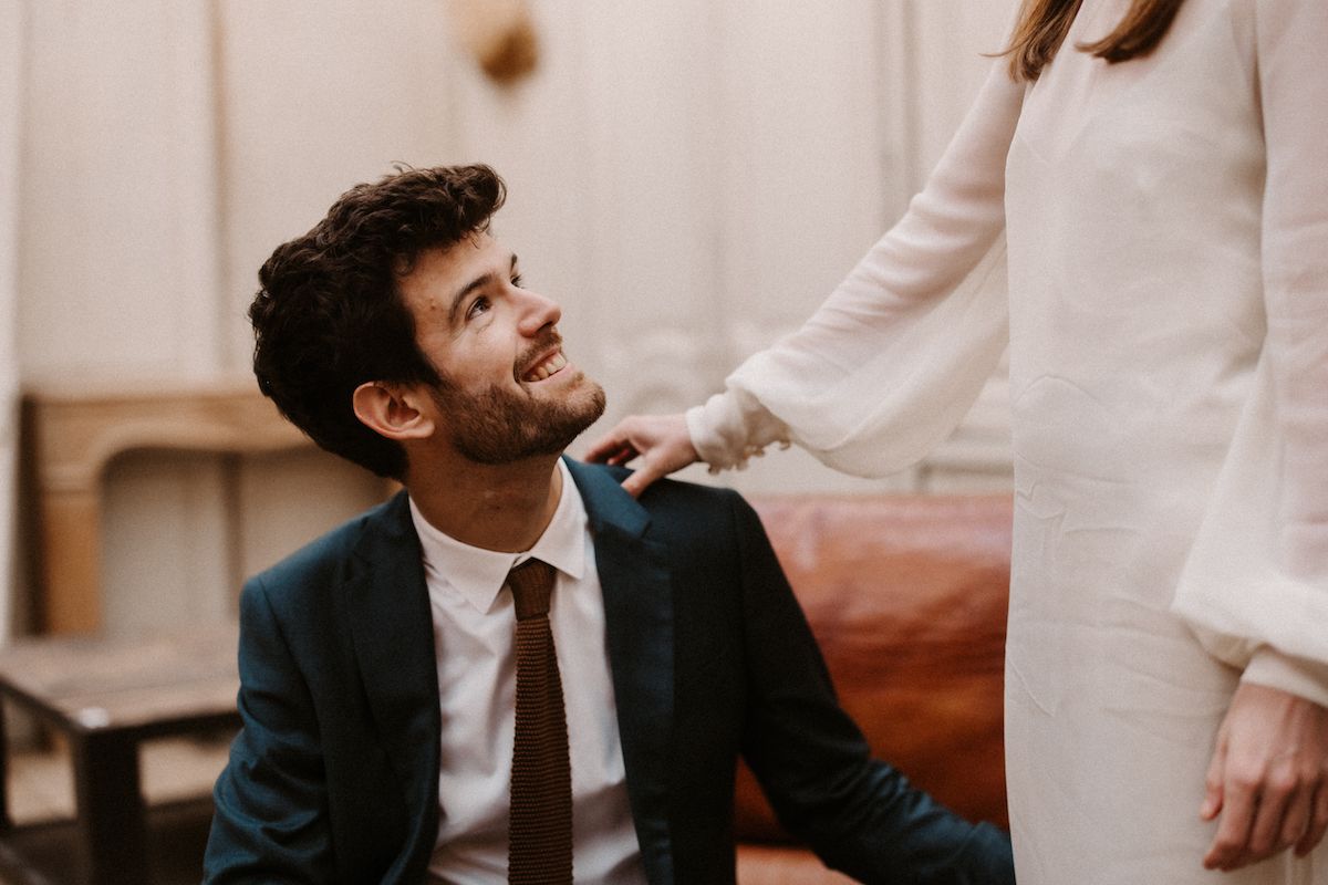 A romantic moment between a couple in elegant attire sitting in a vintage room with warm lighting.