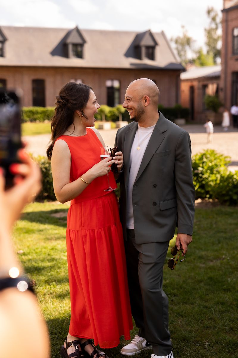 A couple shares a laugh during an outdoor celebration on a lawn with buildings in the background.
