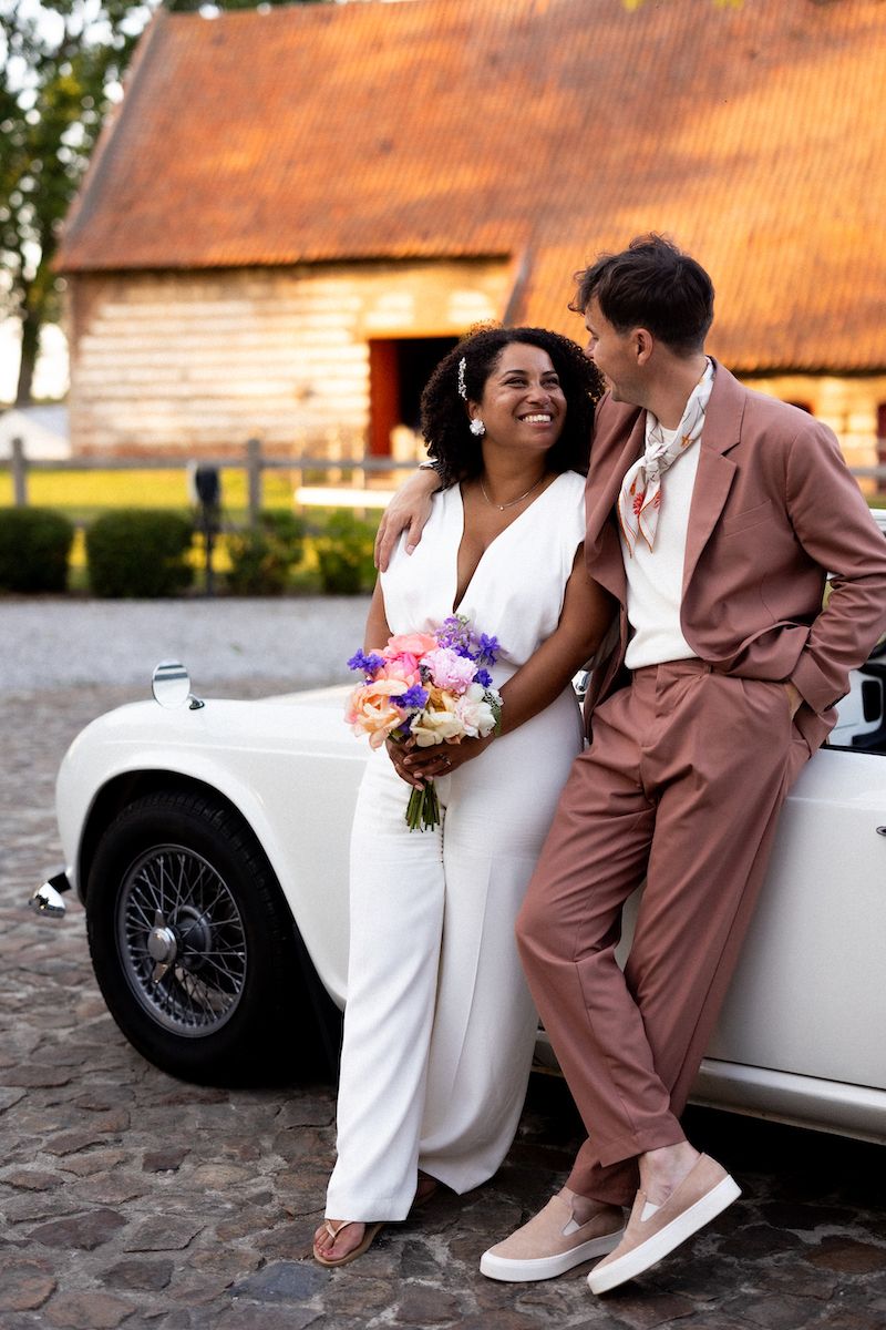 A couple poses by a classic white car with a rustic barn in the background.