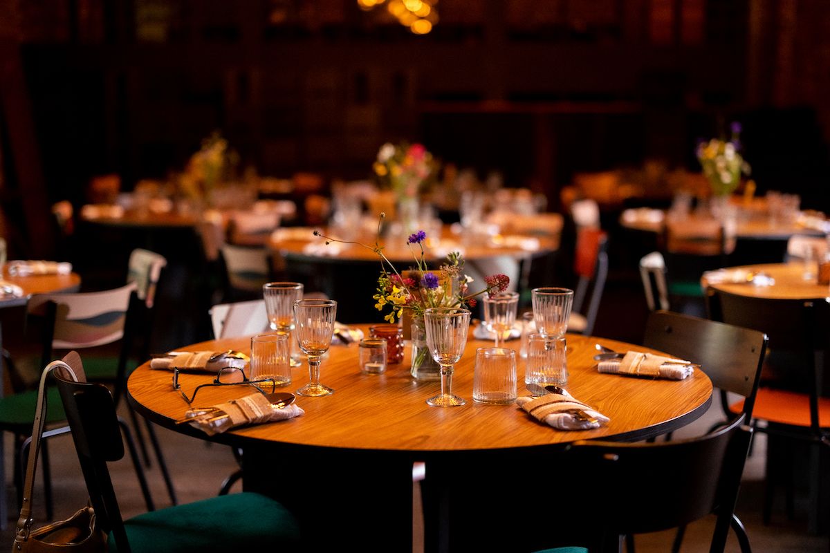 Round wooden tables set for dinner with glasses and place settings in an intimate venue.