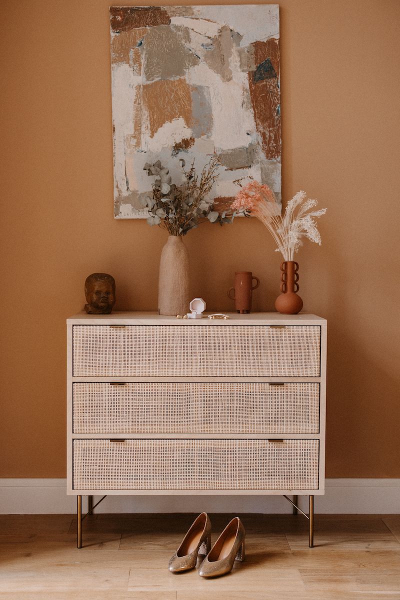 Modern white credenza with brown shoes displayed against a peachy-colored wall with abstract artwork.