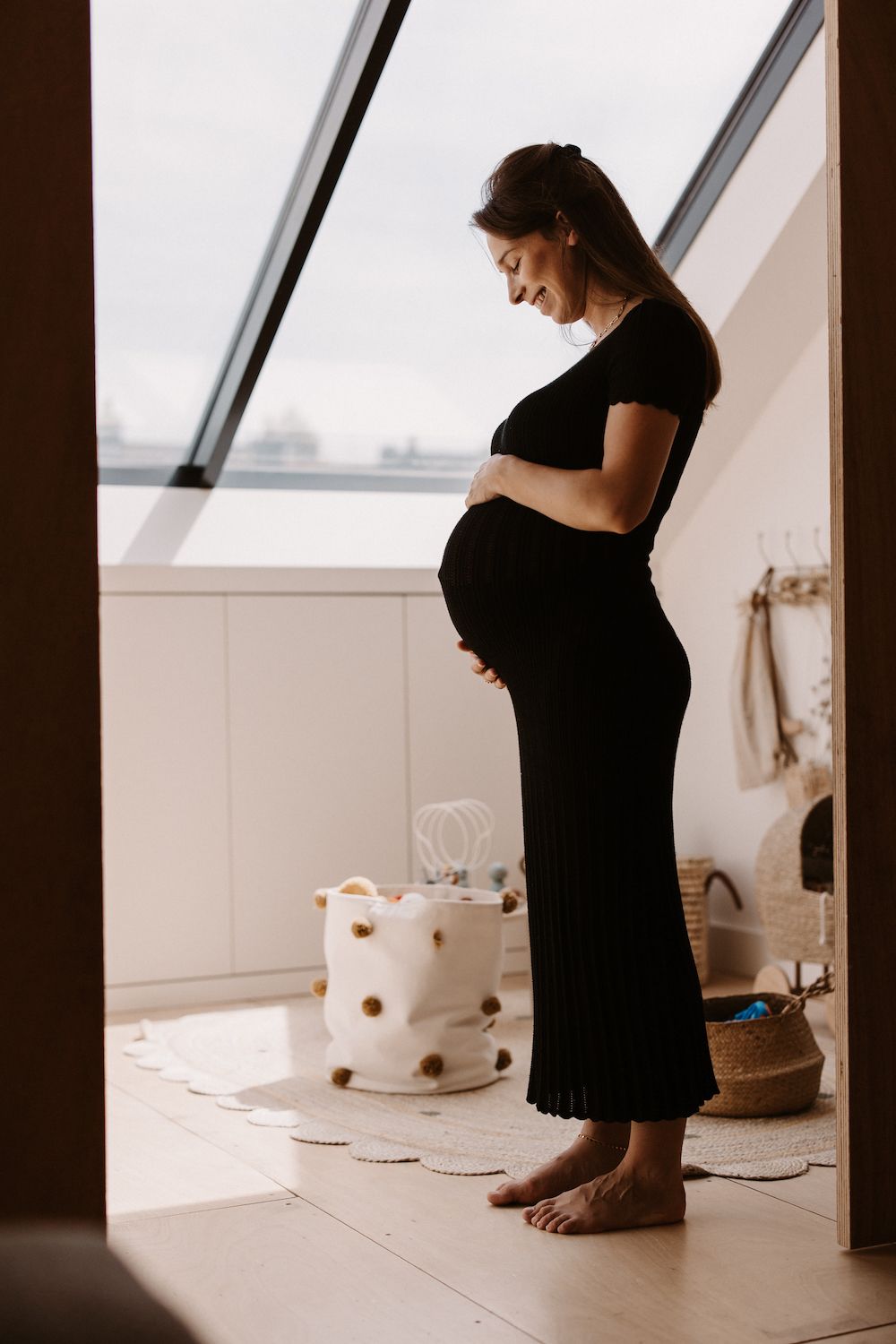 Silhouette of a pregnant figure standing near a window in a black dress.
