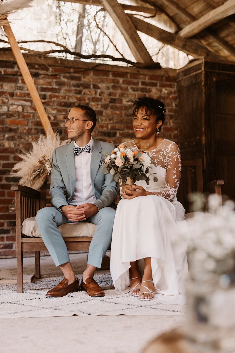 Couple posing in wedding attire in rustic brick setting with dried florals.
