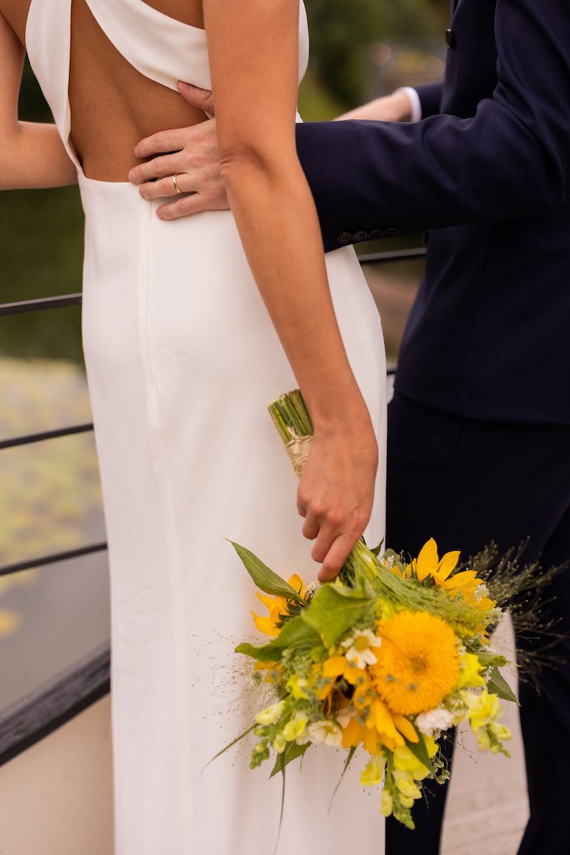 A bride in white holding a vibrant yellow sunflower bouquet against a formal suit.