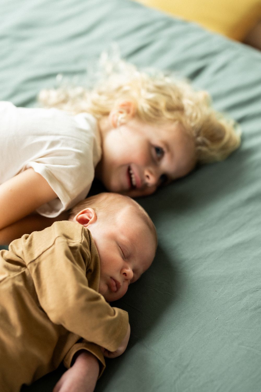 Sweet moment of siblings resting together on mint green bedding.