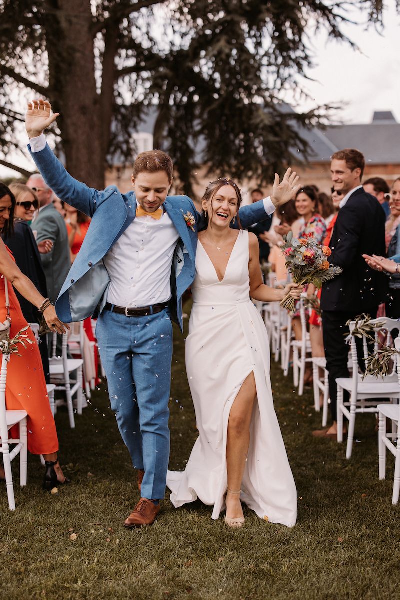 Wedding exit with celebratory crowd and white chairs on lawn.