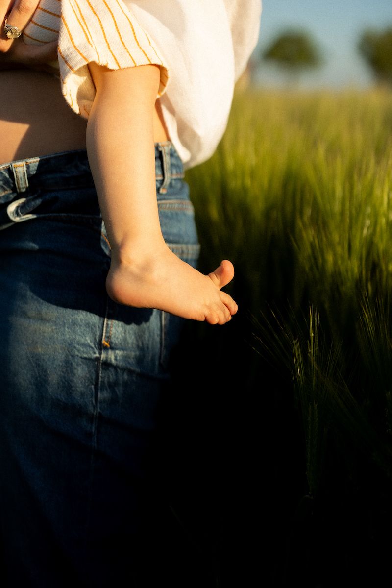 Close-up view of bare feet against tall green grass in summer field.