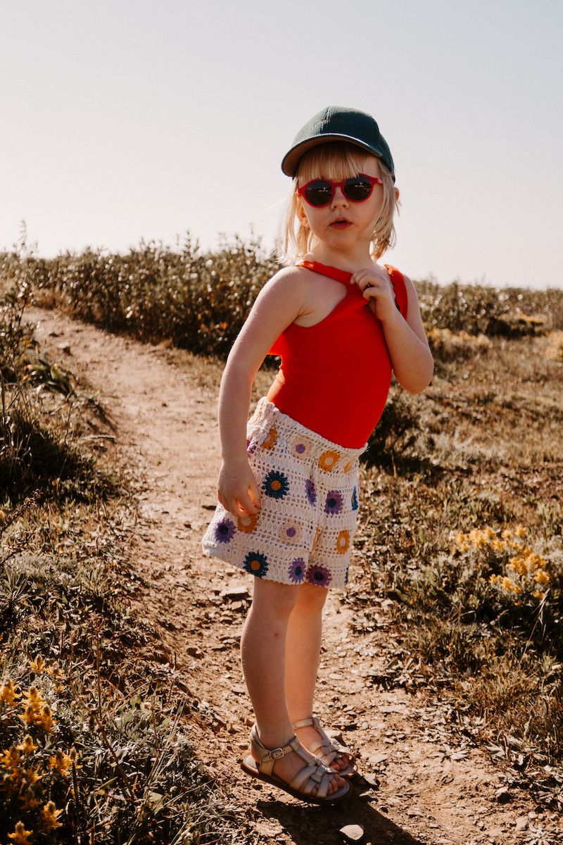 A child in a red top and patterned skirt poses on a sunny dirt path.