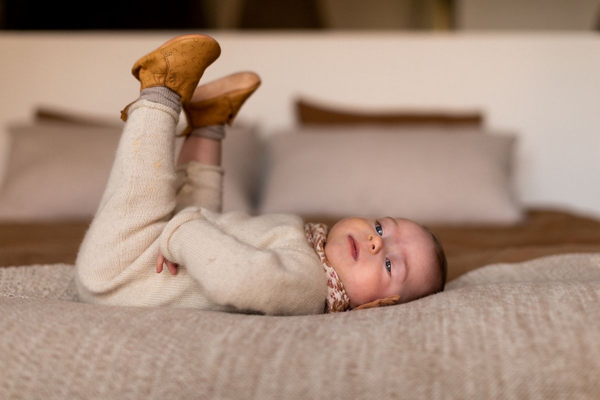 A baby lies peacefully on cream-colored bedding while being cared for.