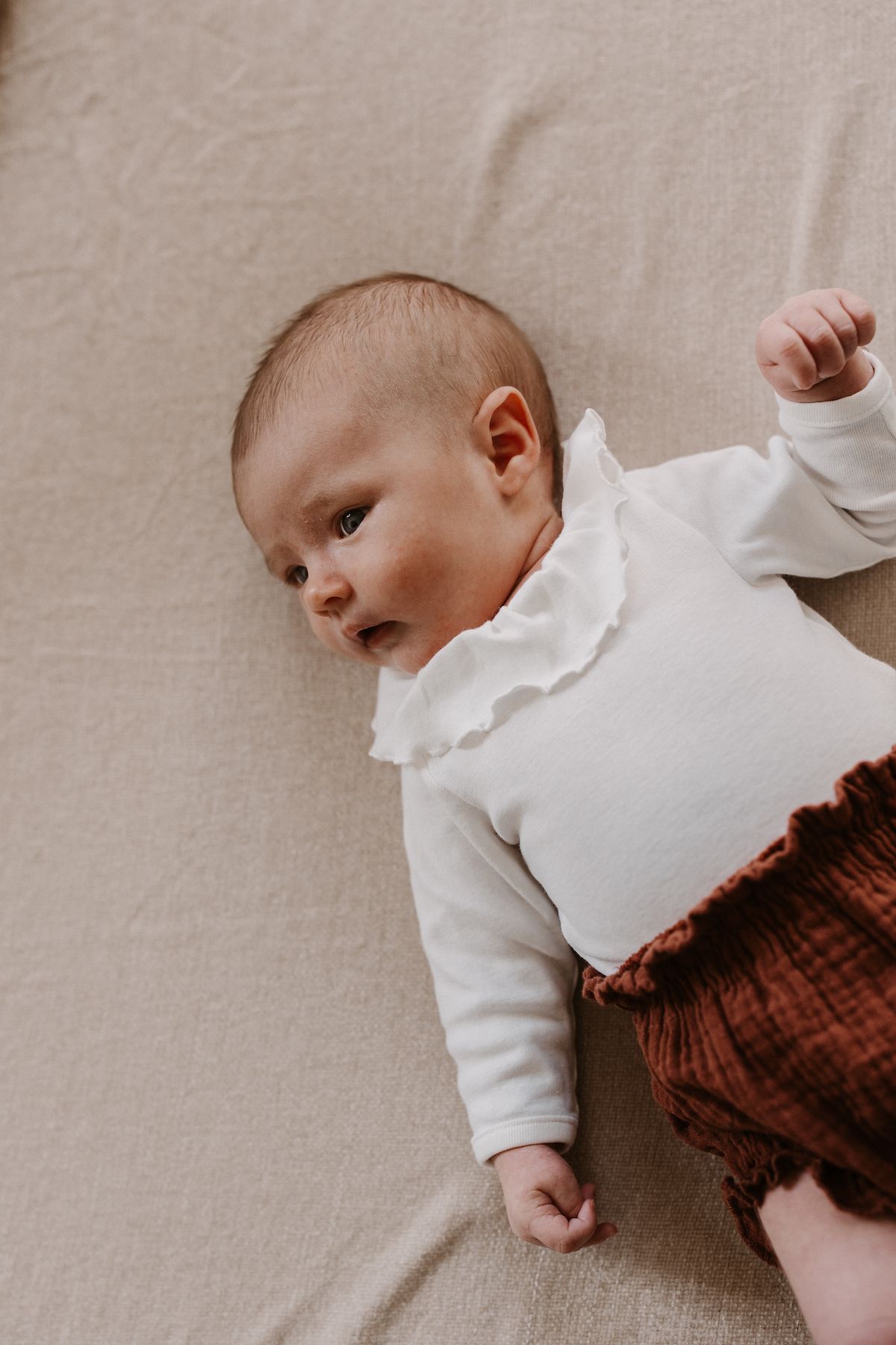 Baby wearing white ruffled top on neutral background.