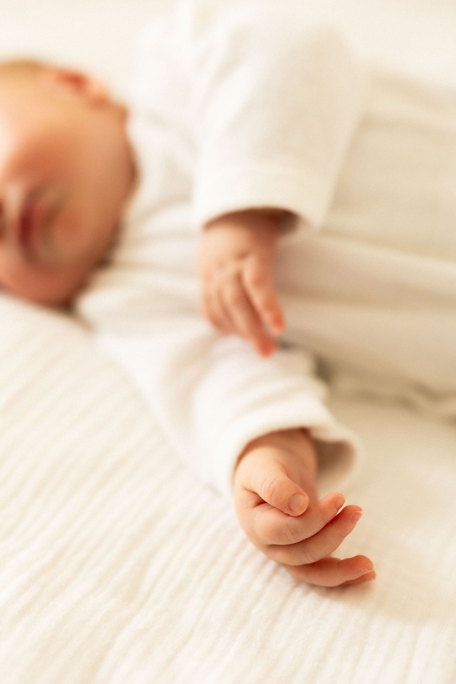 Soft focus image of hands resting on white textured bedding or fabric.