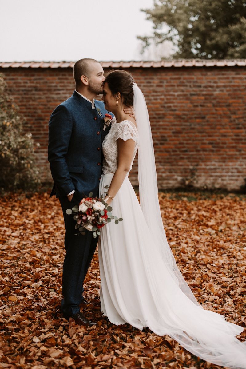 Autumn wedding portrait against a rustic brick wall with fallen leaves.