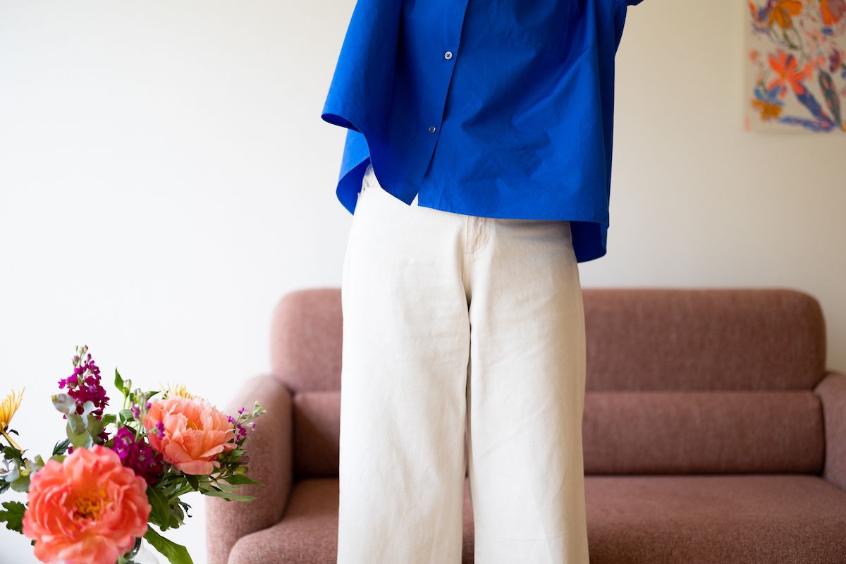 Person in a royal blue blazer and tan pants standing in a contemporary office setting with floral decor.