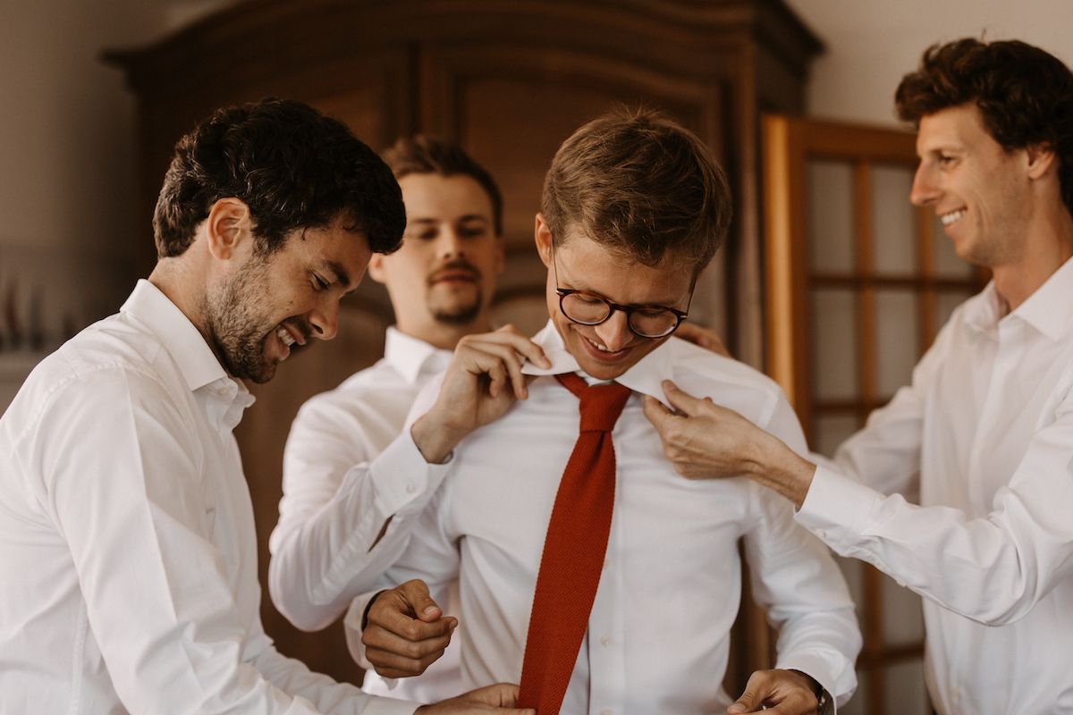 Group of groomsmen in white shirts and red ties sharing a candid moment.