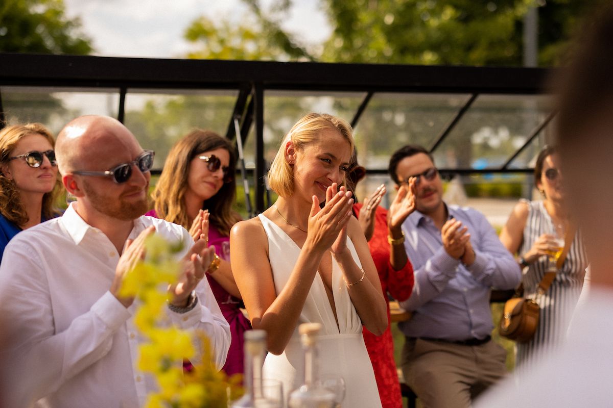 Wedding guests react with surprise and joy while holding drinks during an outdoor celebration.
