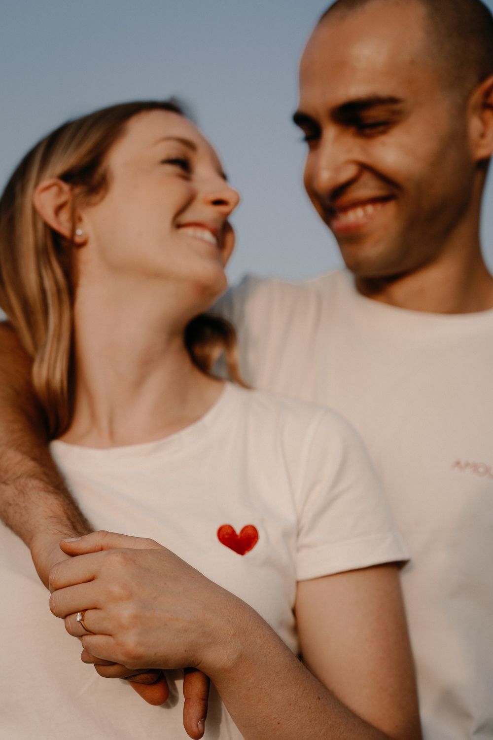 Romantic couple wearing matching white shirts embracing in golden sunlight.
