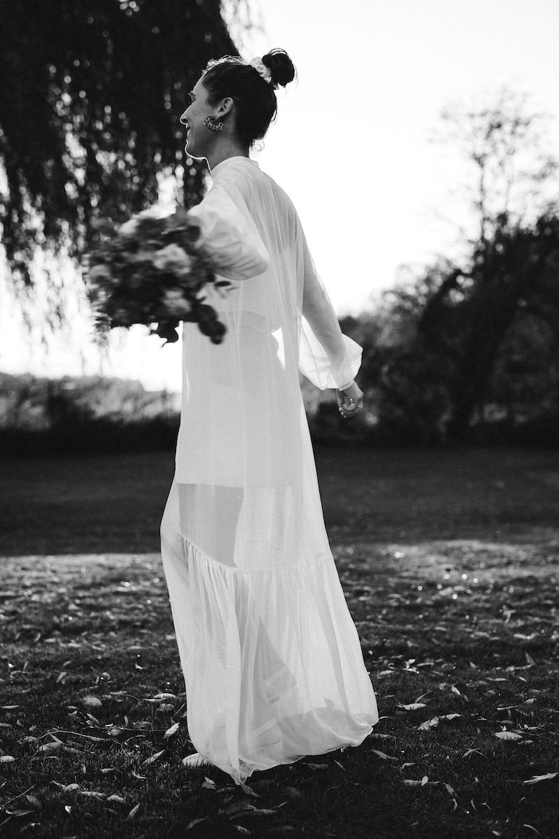 Black and white portrait of bride twirling in flowing white dress at sunset.