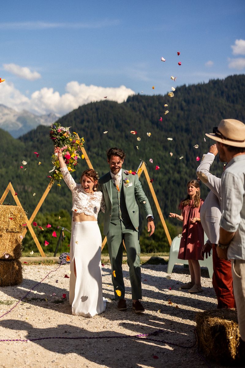 Festive outdoor mountain wedding celebration with flower petals being tossed in the air.