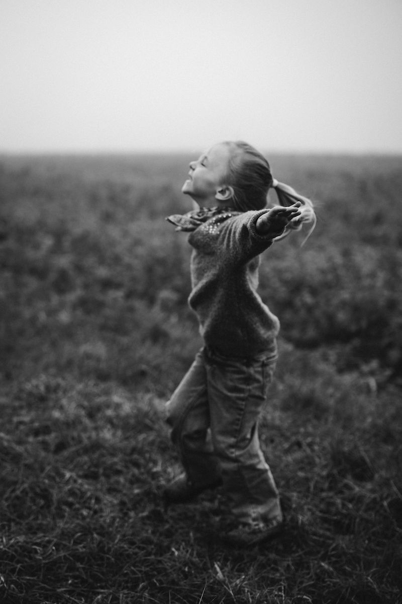 Black and white photo of small child with arms spread wide in an open field.