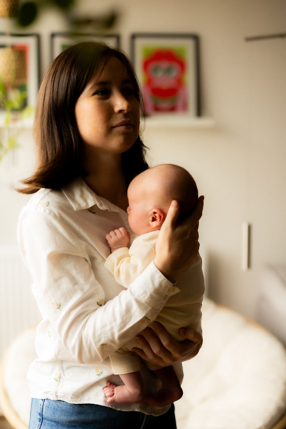 A white-clothed figure holds and nurtures a baby in a room with art on the walls.