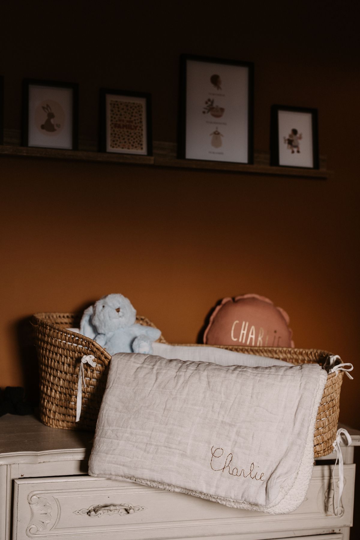 Nursery shelf with framed artwork and stuffed animal in woven basket.