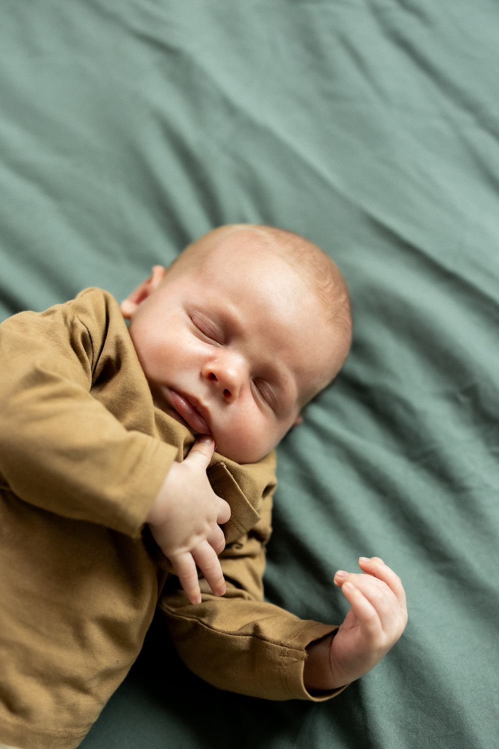 Sleeping baby in brown outfit lying on mint green bedding.