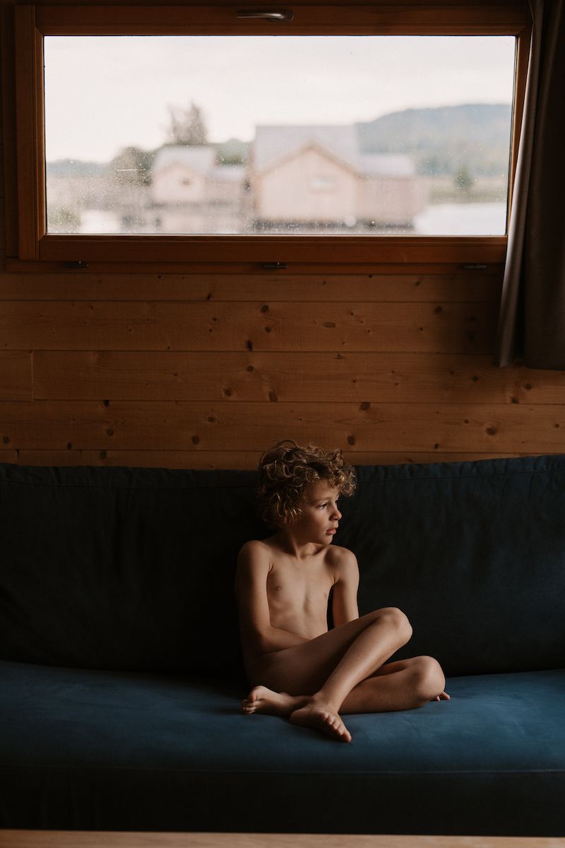 A child sitting on a blue couch beneath a window in natural light.