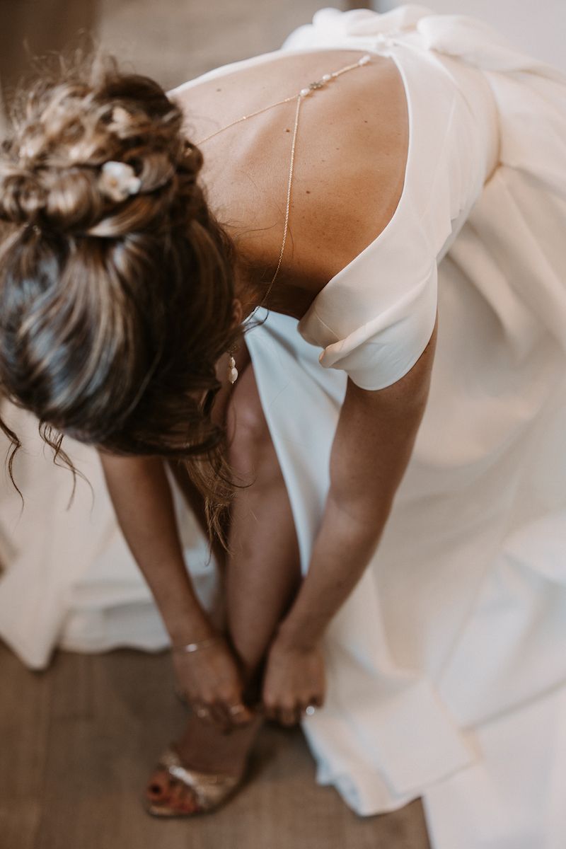 Close-up of a bride adjusting her shoe while wearing a flowing white wedding dress.