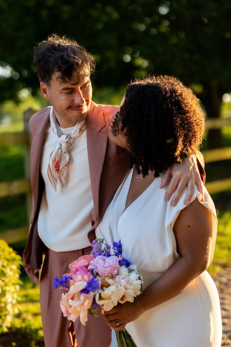 A couple shares an intimate moment in golden sunlight with a colorful bouquet.