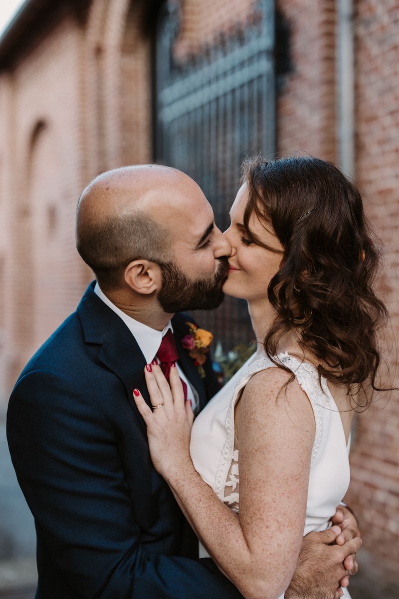 A romantic wedding portrait featuring couple sharing tender kiss against industrial brick backdrop.