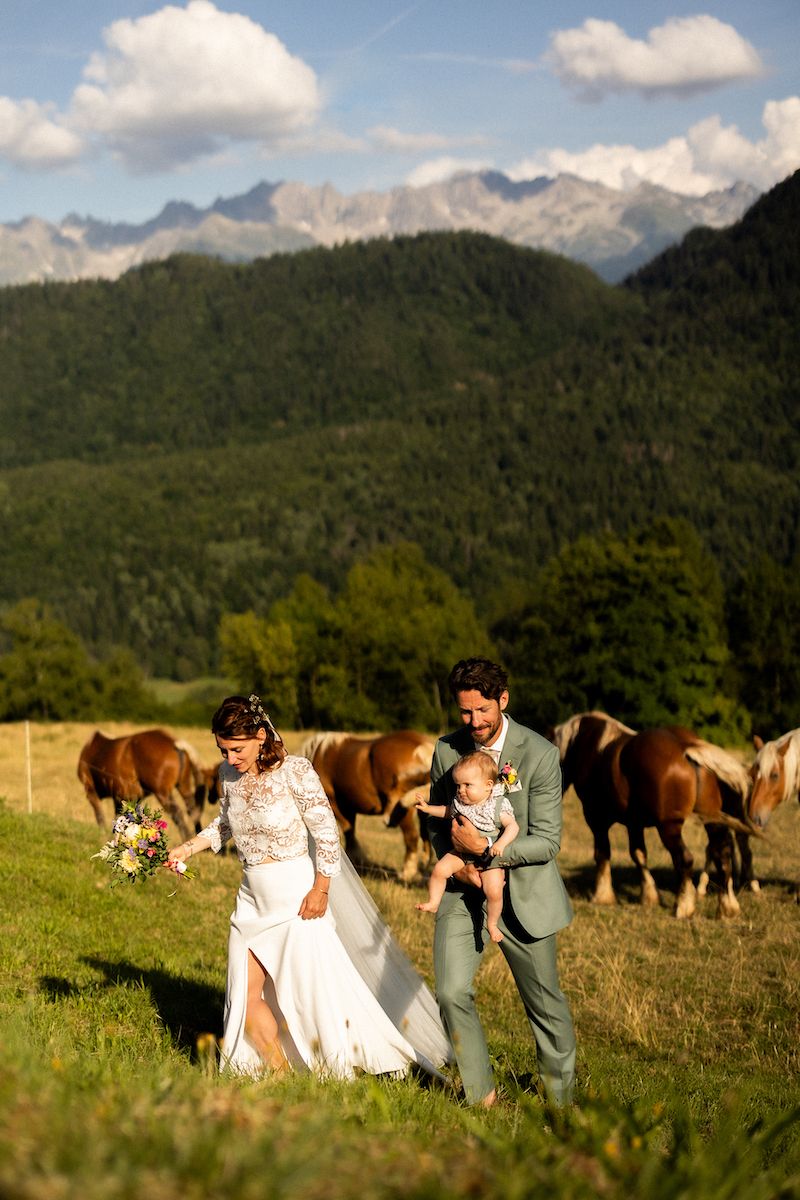 Wedding couple walking in mountain meadow with horses grazing in background.