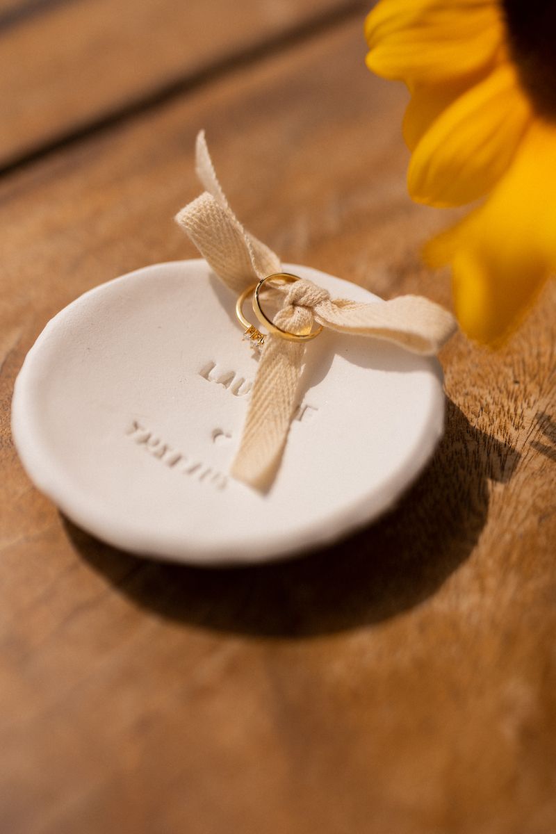Close-up of delicate white ceramic ring dish with cream ribbon on wooden surface.