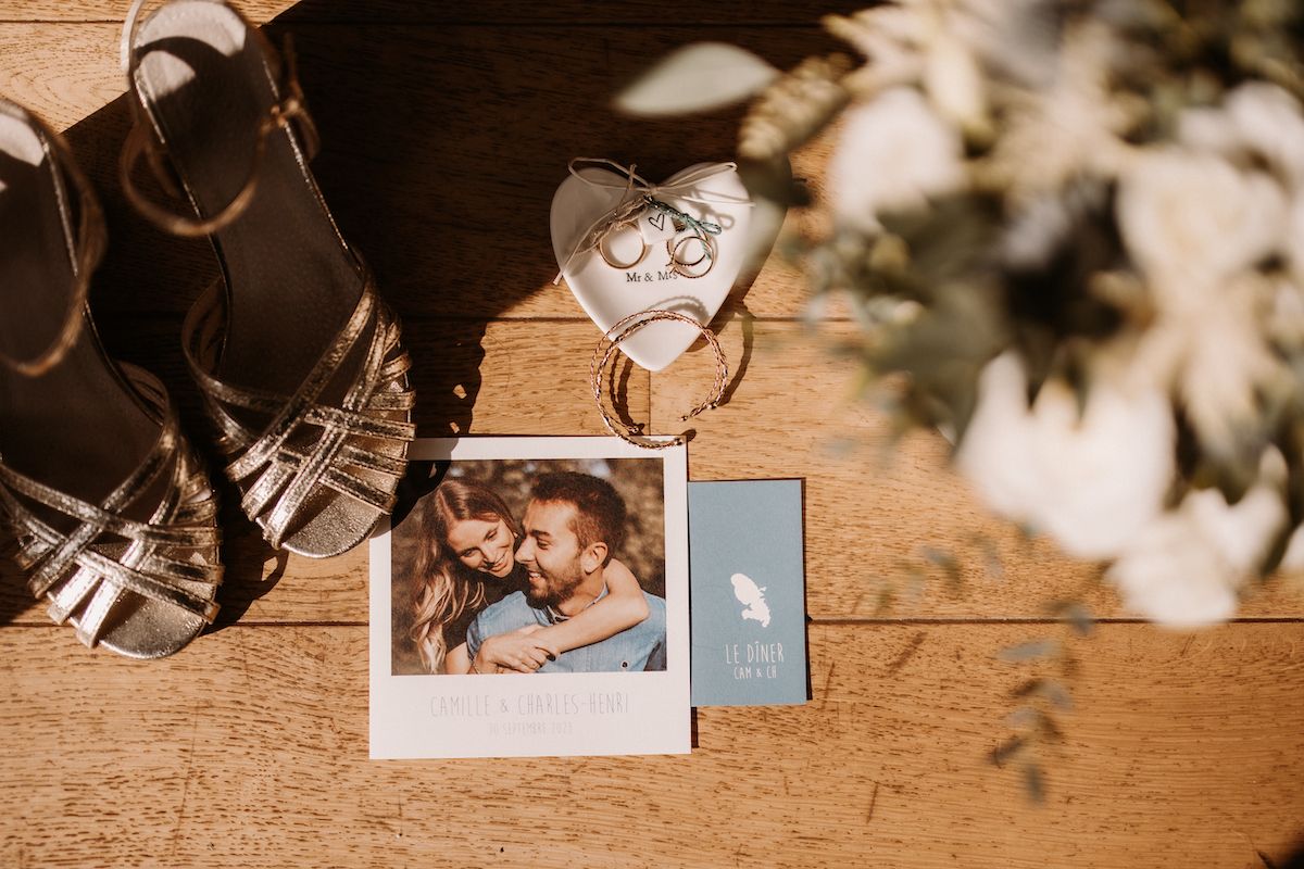 Wedding photos and rings arranged on a rustic wooden surface with sunlit shadows.