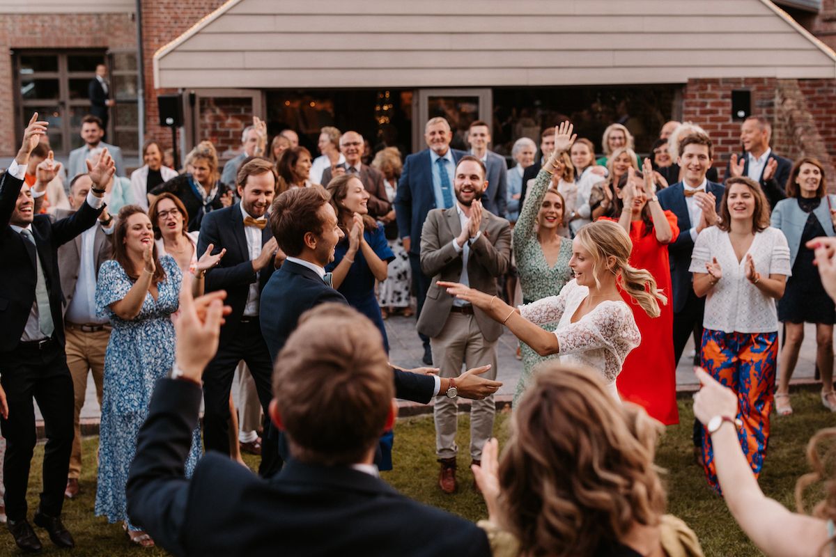 Wedding guests cheering and celebrating on a lawn outside a brick building.