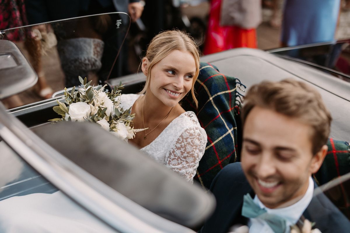 Newlyweds sharing joyful moment in classic car with wedding florals.