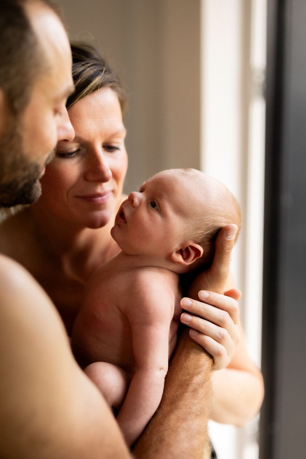 Tender family moment with newborn baby by sunlit window.