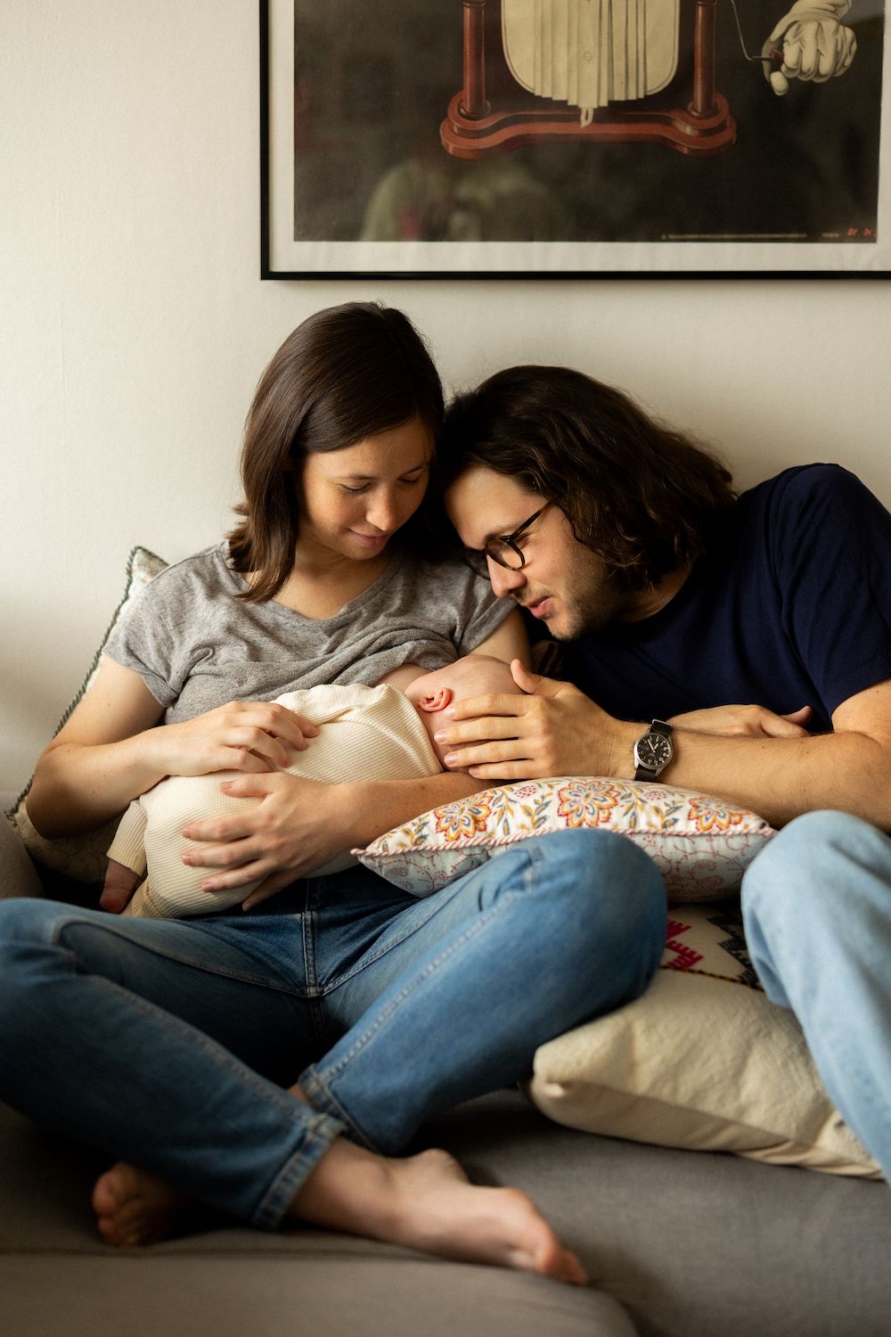 Couple resting together on a cozy gray couch with their infant.