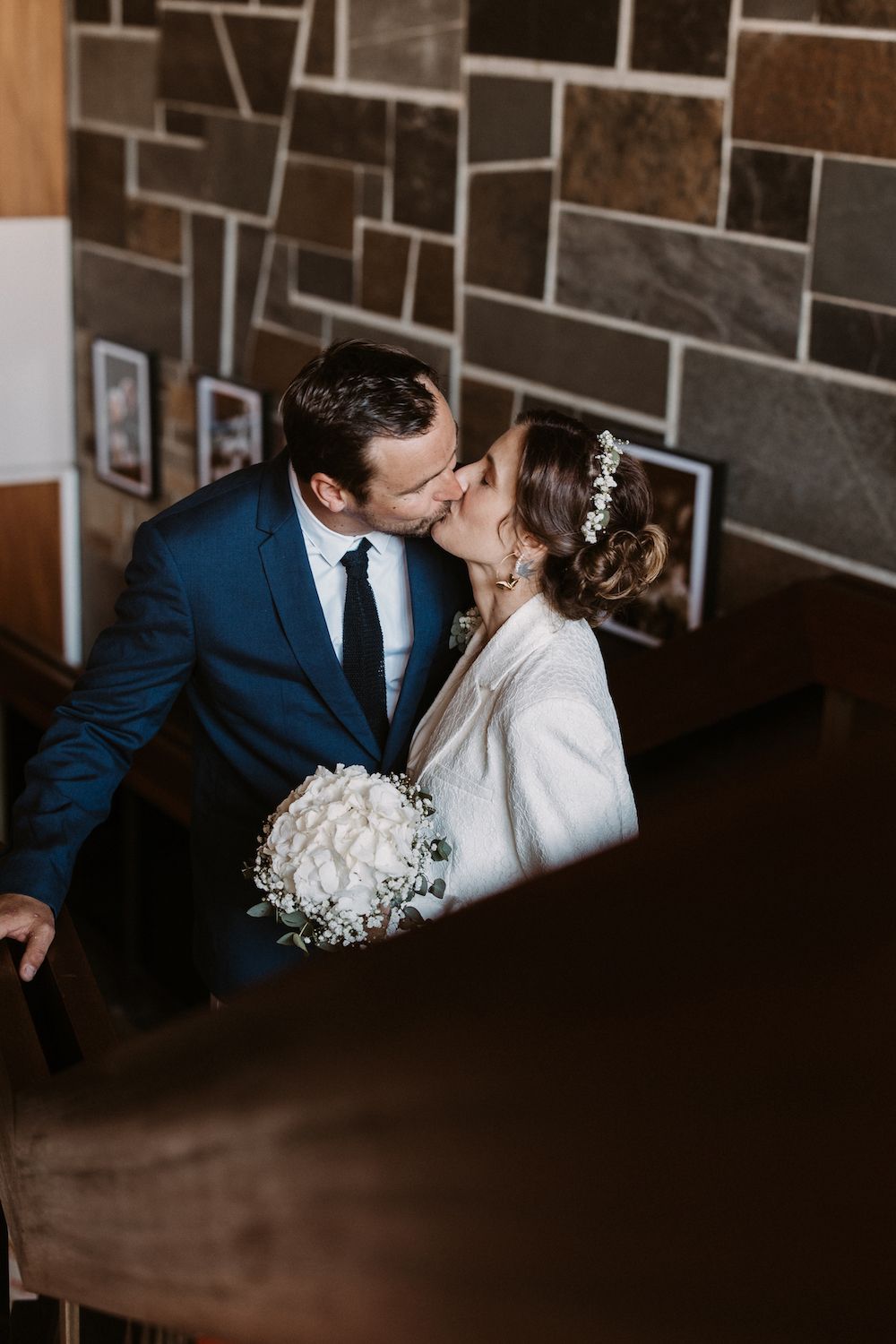 Intimate wedding portrait with couple against stone wall in warm lighting.