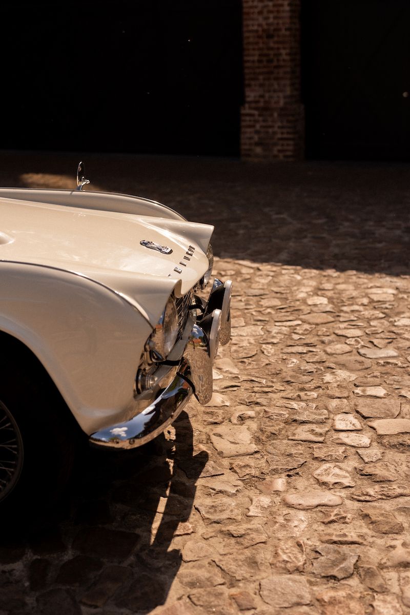 Front view of a classic white vintage car on cobblestone pavement in dramatic lighting.