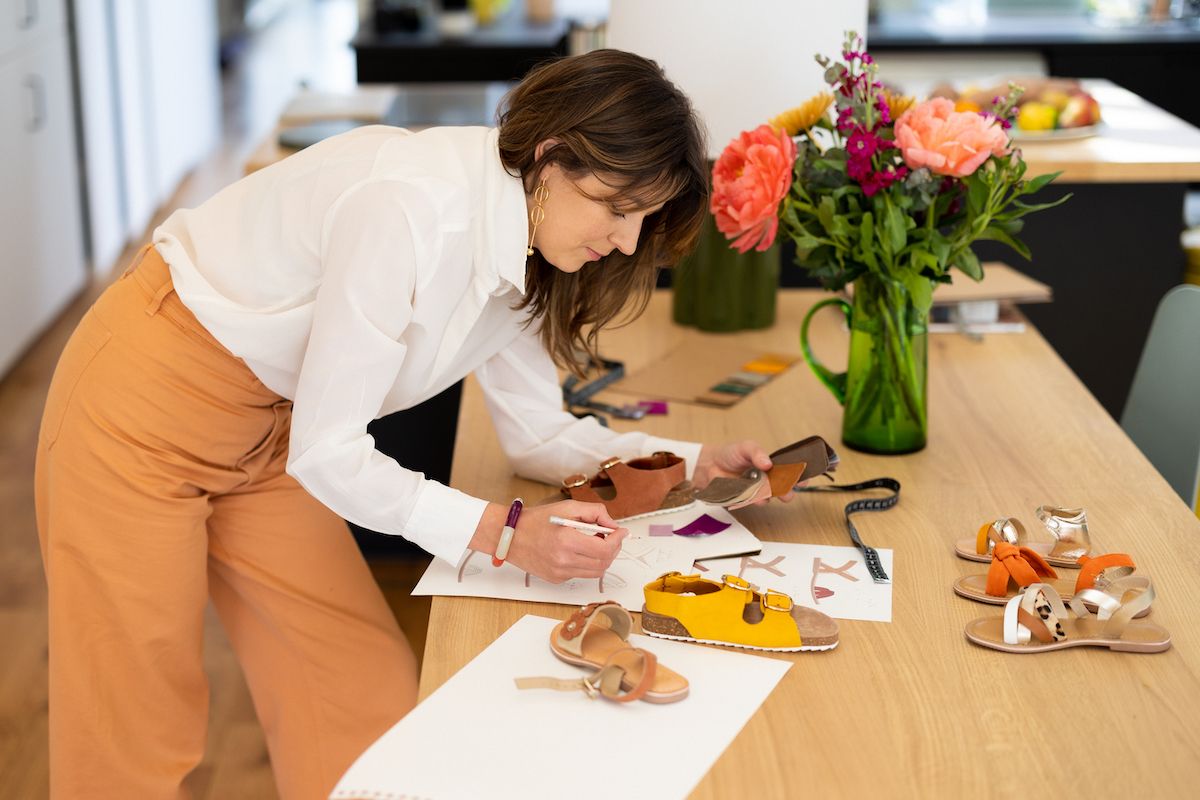 Hands writing or drawing on a wooden desk surface next to coral-colored flowers.