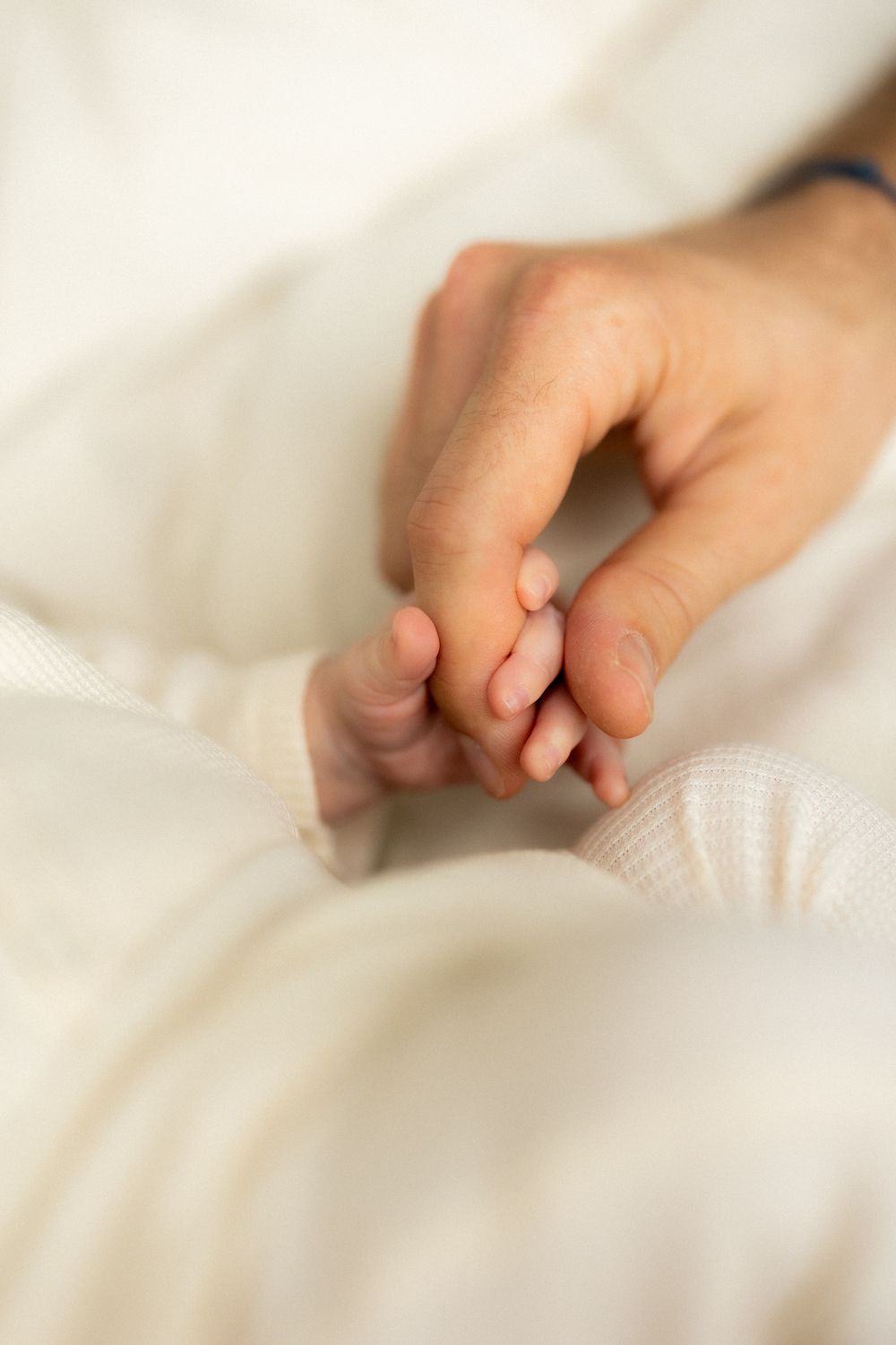 Delicate baby fingers and toes photographed against white bedding in soft focus.
