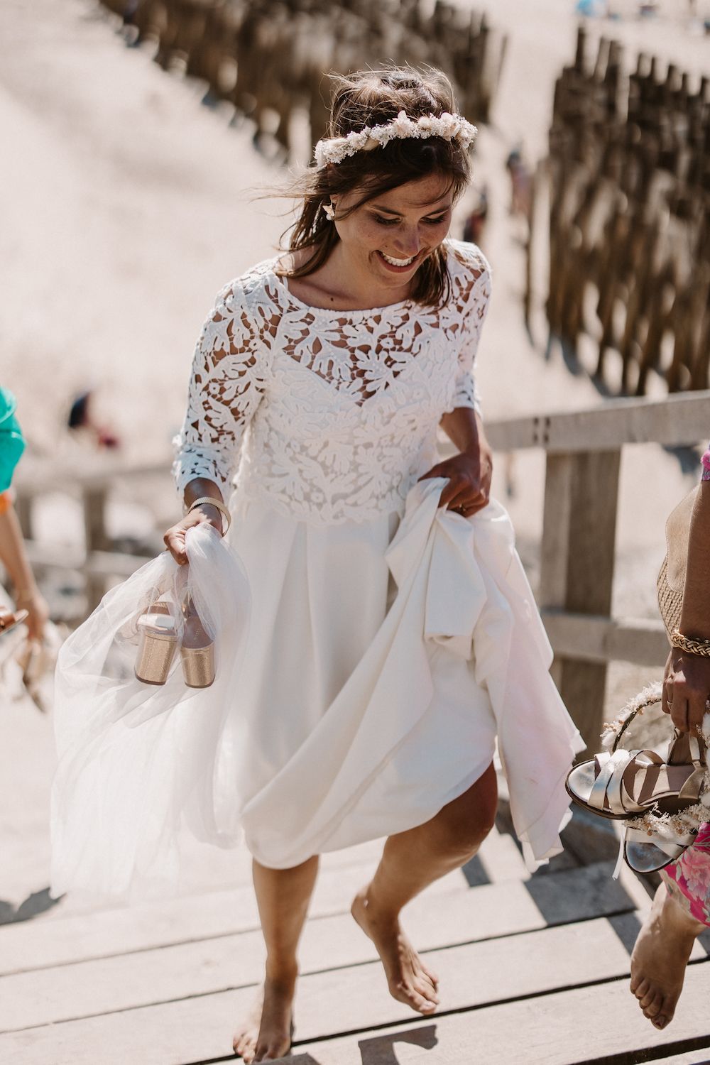 Bride in lace detail dress walking along sunny pathway.
