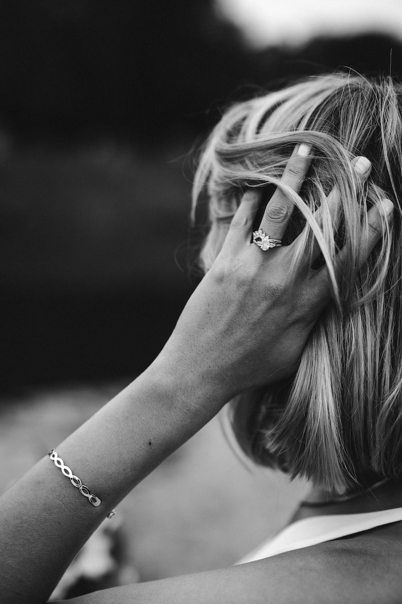 A close-up black and white shot of a hand with an engagement ring running through blonde hair.