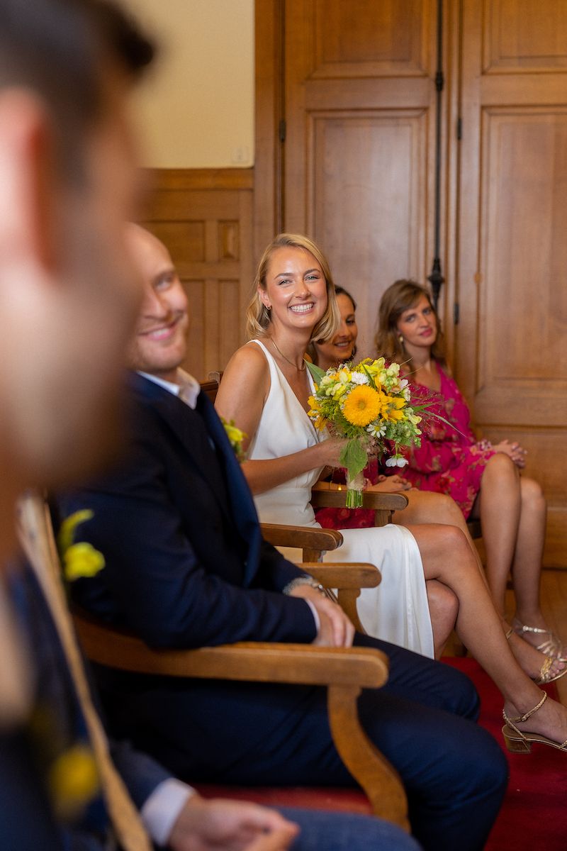People in formal attire sitting in chairs during a wedding ceremony.