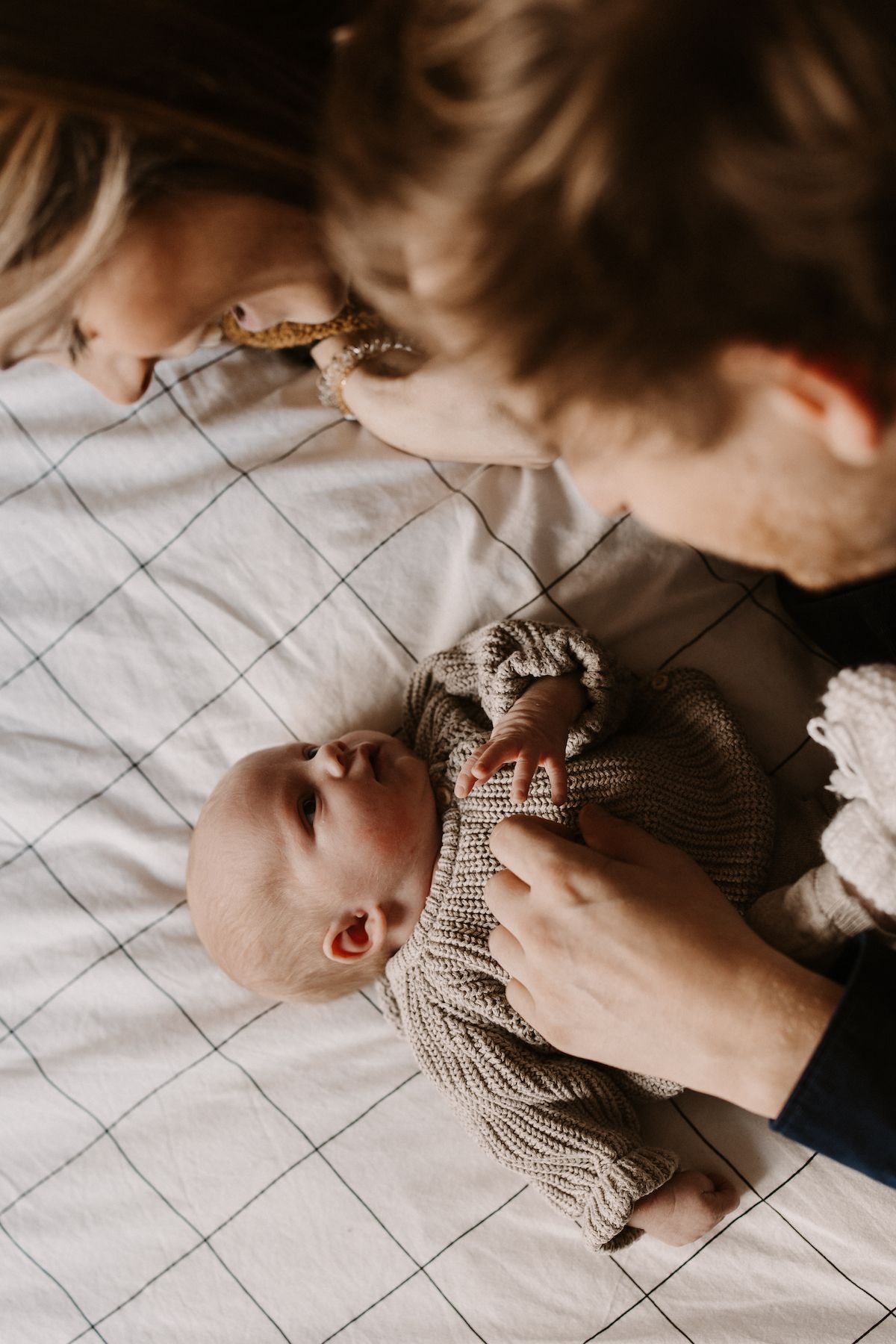 Overhead view of caregiver dressing infant in knit sweater on quilted surface.