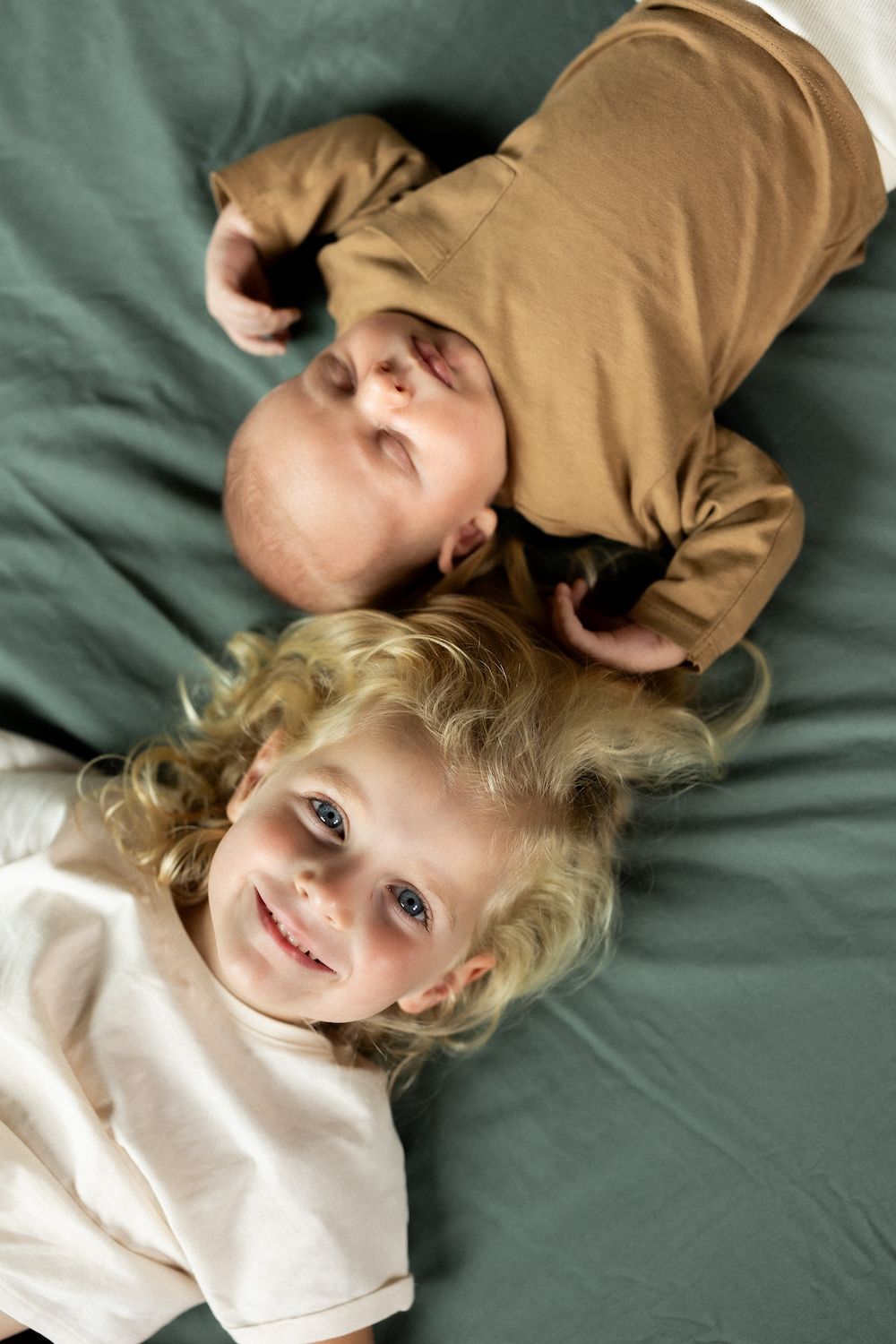Siblings lying head to head on mint green bedding, sharing a tender moment.