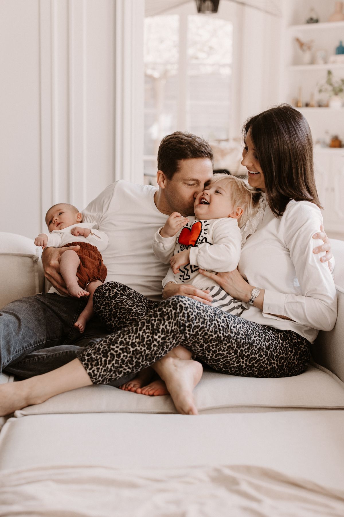 Family cuddles together on a cozy couch in natural light.