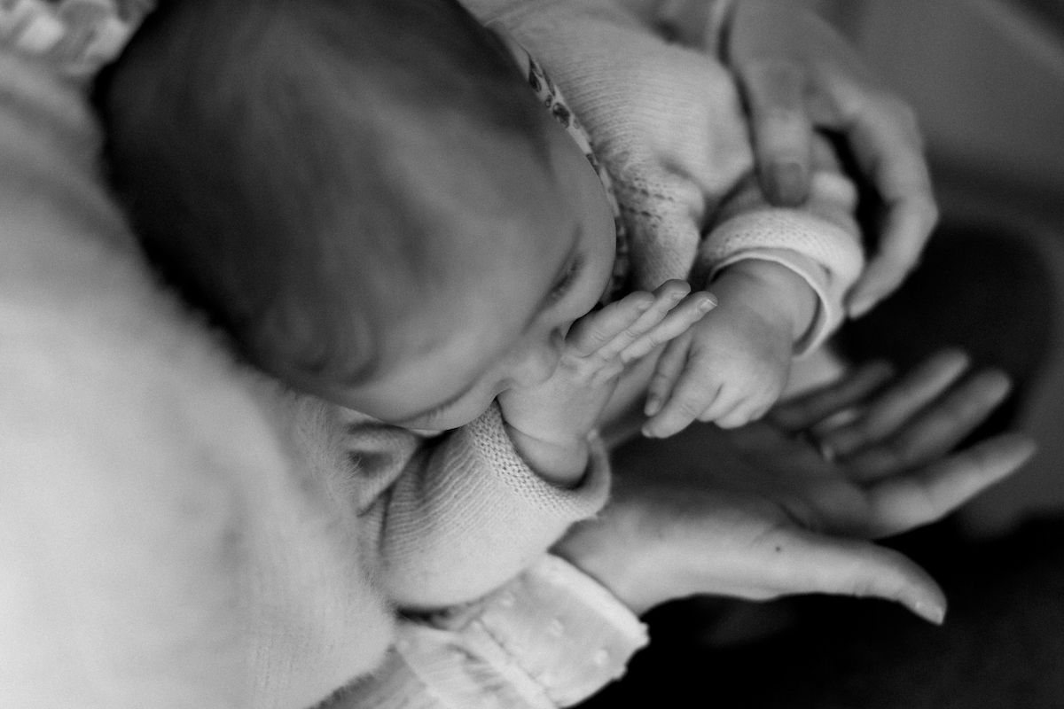 Intimate black and white close-up of gentle hands caring for an infant.